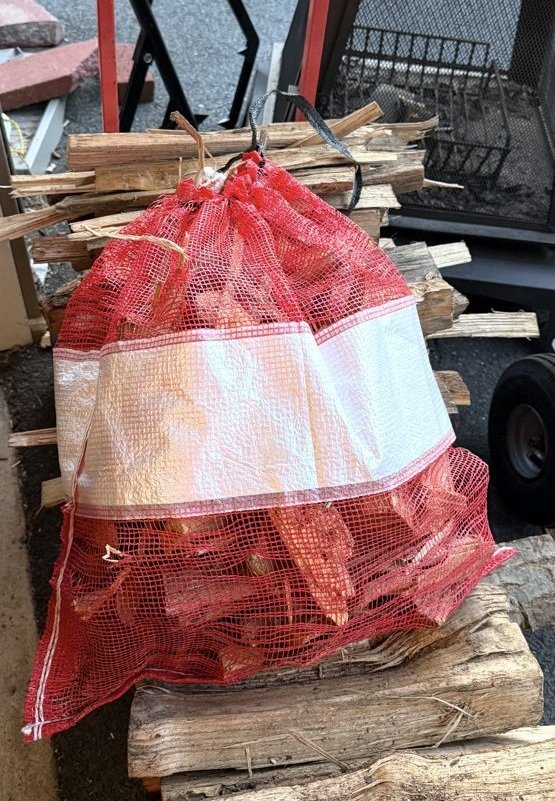 A mesh bag of kindling stacked on split firewood, ready for delivery