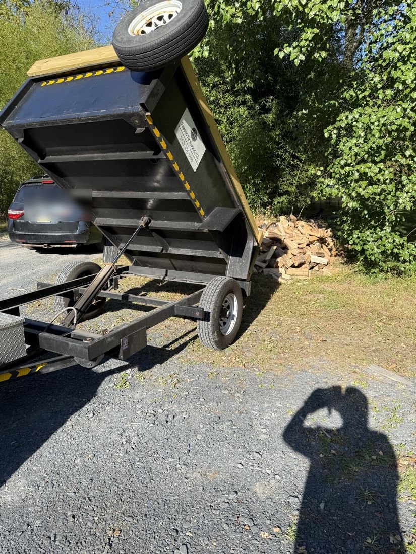 A dump trailer tipped up, unloading split firewood next to a driveway
